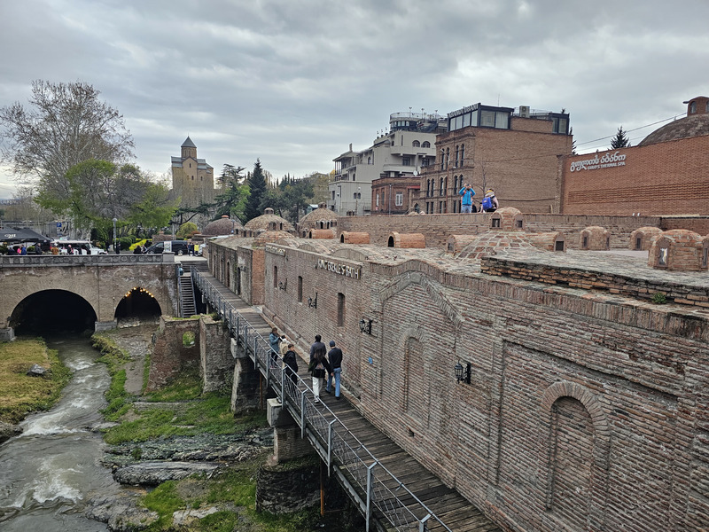 People walking along a bridge beside the Abanotubani sulfur baths and stream in Tbilisi, Georgia.