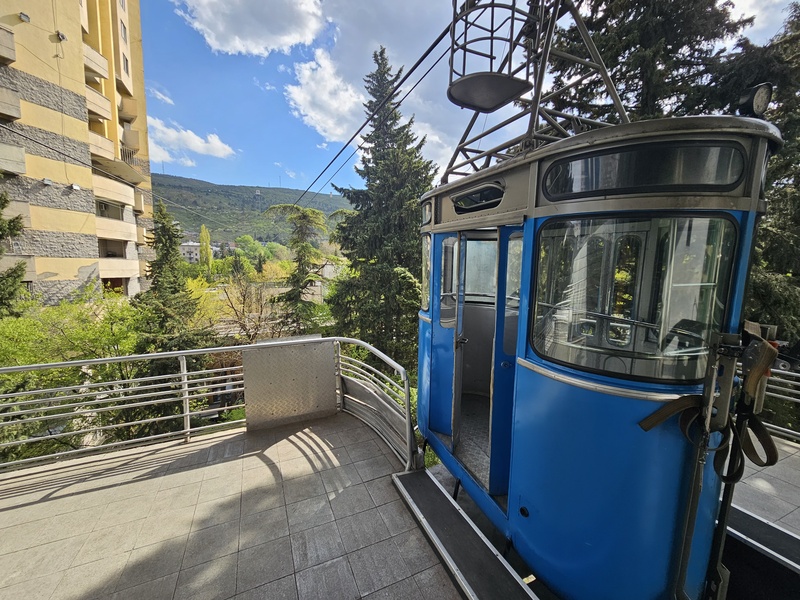 A blue vintage cable car hanging at a station platform in Tbilisi, with the other end in the far background.