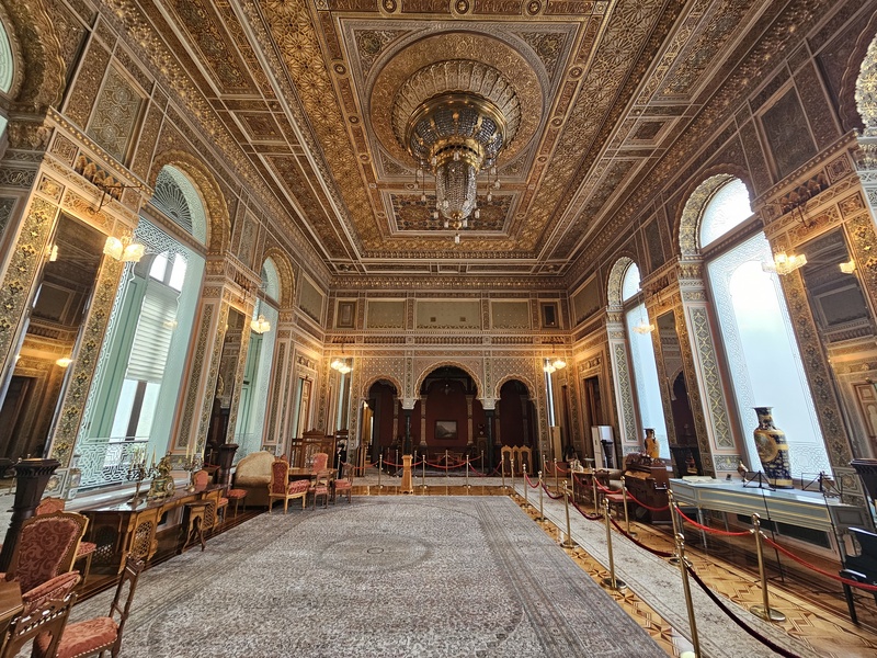 Interior of National Museum of History of Azerbaijan in Baku featuring a large patterned rug, gold-leafed ceilings, arched windows, and roped-off furniture.