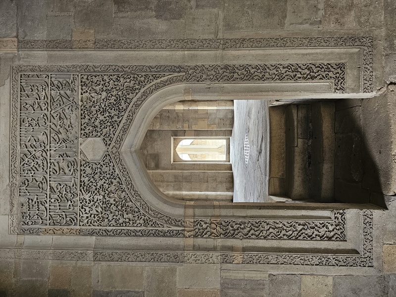 Intricate stone carvings featuring Arabic calligraphy and floral patterns frame an arched window in the Palace of the Shirvanshahs in Baku.