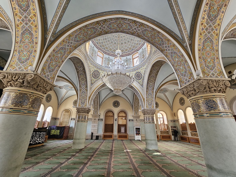 Interior of a mosque in Baku featuring ornate arches, intricate tile work, and a large chandelier hanging from a domed ceiling.