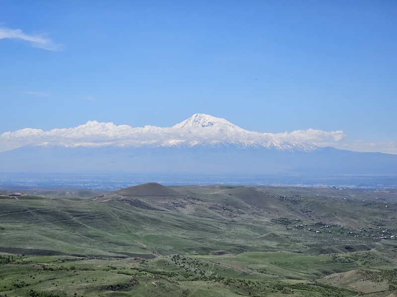 Mount Ararat rising above the green rolling hills near Yerevan, Armenia, under a clear blue sky.