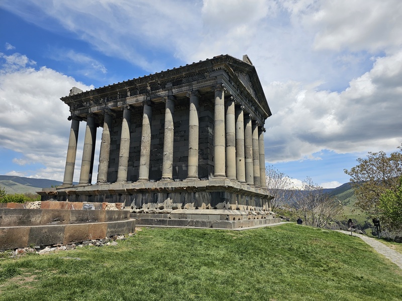 The ancient Roman-style Garni Temple in Garni, Armenia, featuring tall stone columns and a triangular pediment against a blue sky with clouds.