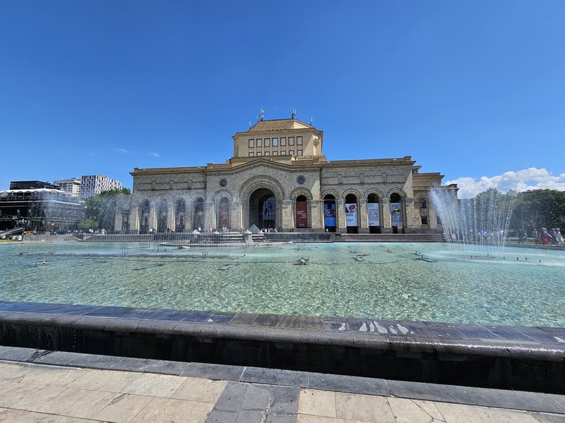 The National Gallery in Yerevan, Armenia, featuring a large fountain in the foreground and a clear blue sky.