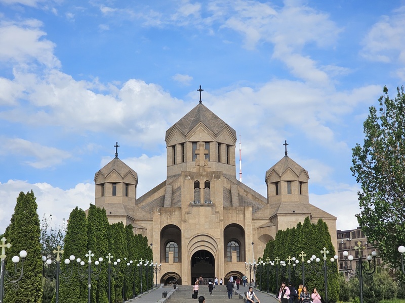 The Saint Gregory The Illuminator Cathedral in Yerevan, Armenia, featuring its distinctive stone architecture and three domes under a blue sky with scattered clouds.