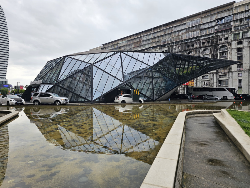 Glass McDonald's building reflected in a pool in Batumi, Georgia, with apartment blocks behind it.