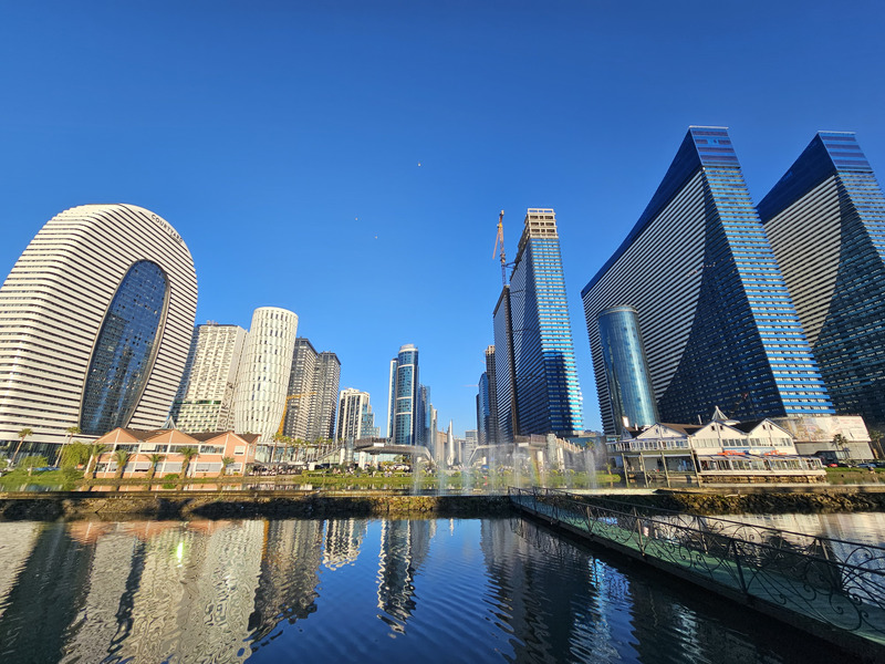 Modern Batumi waterfront towers reflected in the water under a clear blue sky.