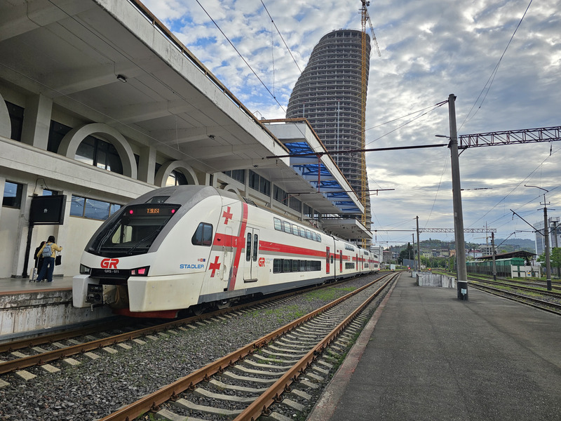 Georgian Railways train at Batumi station under overhead wires and a cloudy sky.