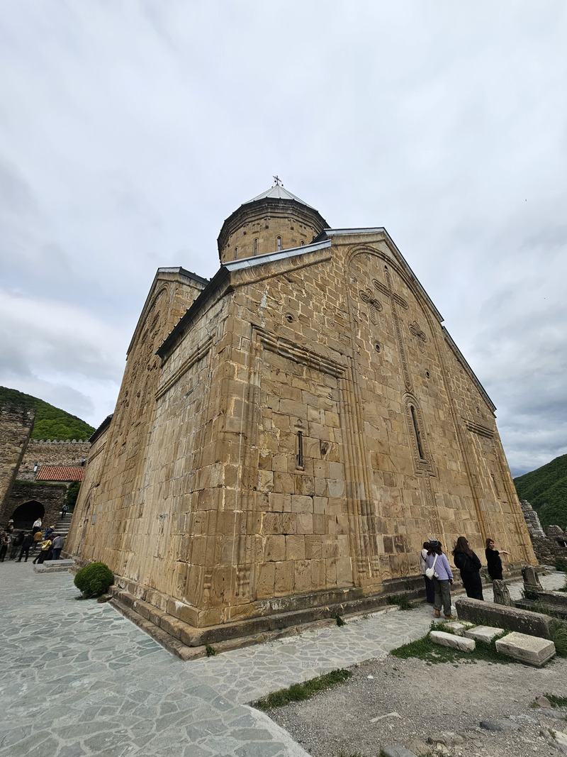 Stone exterior of the Church of the Assumption of the Virgin Mary within the Ananuri Fortress Complex under a cloudy sky.