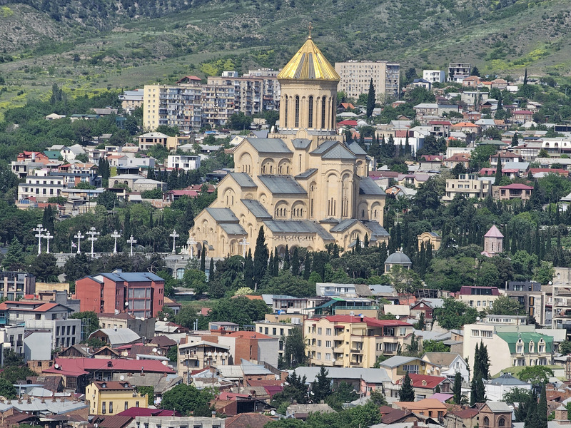 Holy Trinity Cathedral of Tbilisi rising above the city with green hills behind it.