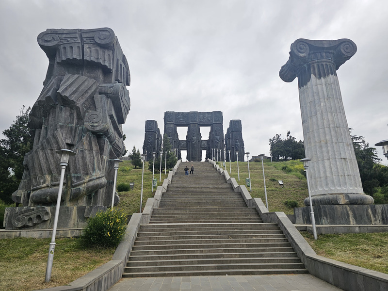 Monumental columns of the Chronicle of Georgia in Tbilisi under an overcast sky.