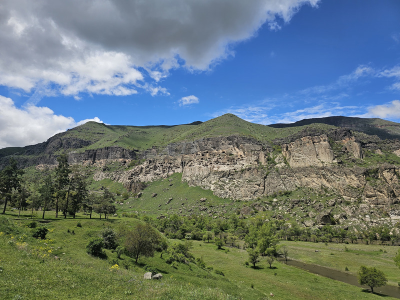 Vardzia cave monastery carved into rocky green hills under a cloudy blue sky