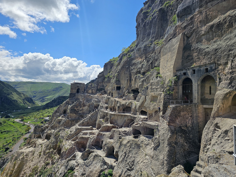 Cave monastery chambers and stairways carved into the cliffs at Vardzia, Georgia, under a blue sky.