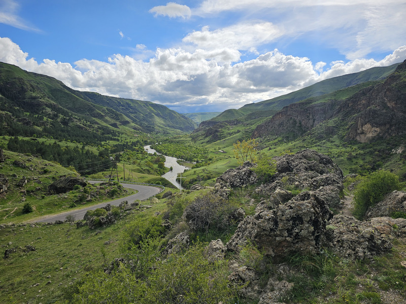 Green mountain valley near Vardzia with a winding river and road under dramatic clouds.