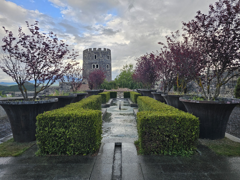 Stone tower and landscaped garden at Rabati Castle in Akhaltsikhe under a cloudy sky.
