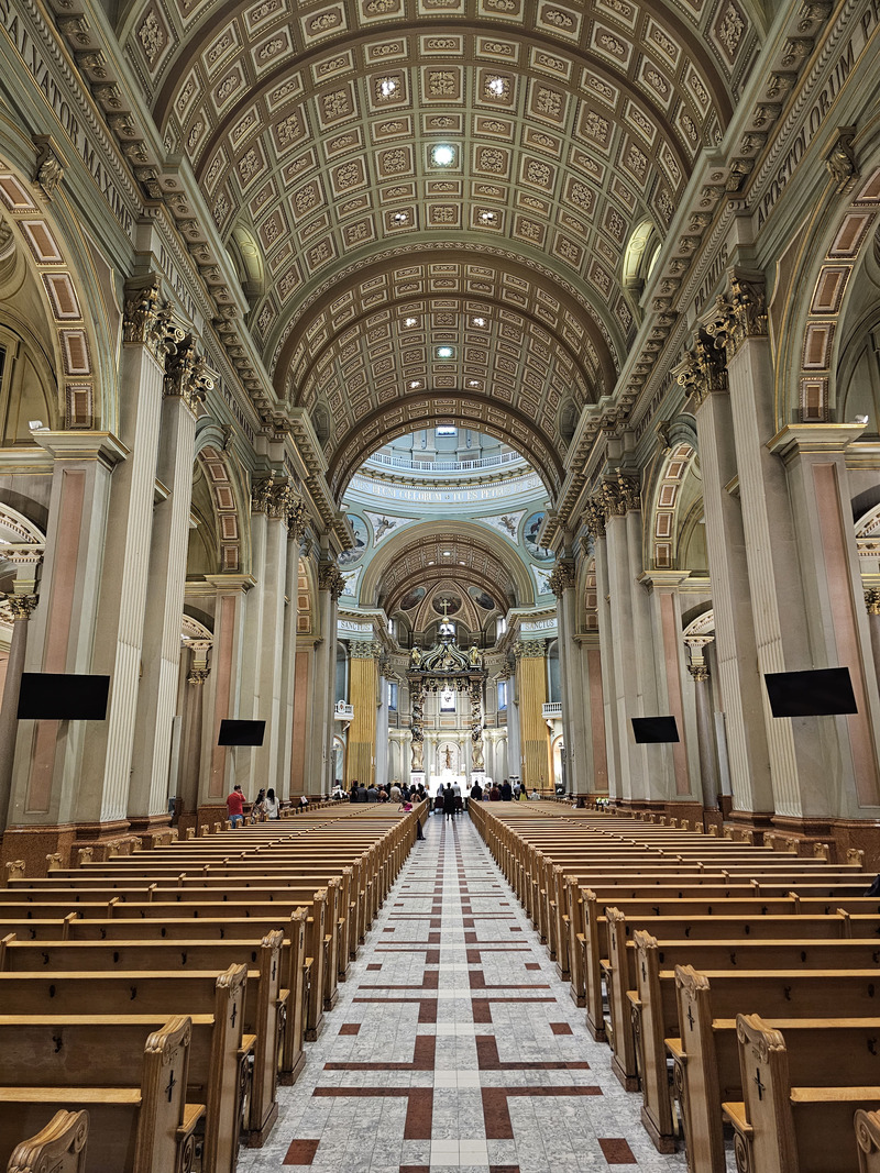 The central aisle of Mary, Queen of the World Cathedral, lined with wooden pews and tall columns beneath an ornate coffered ceiling.