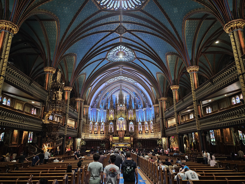 Notre-Dame Basilica's blue ceiling dotted with gold stars above carved galleries, wooden pews, and an illuminated blue-and-gold sanctuary.
