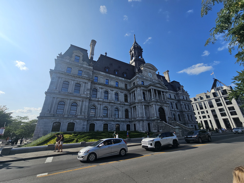 The ornate stone facade, steep roof, and clock tower of Montreal City Hall beneath a blue sky.