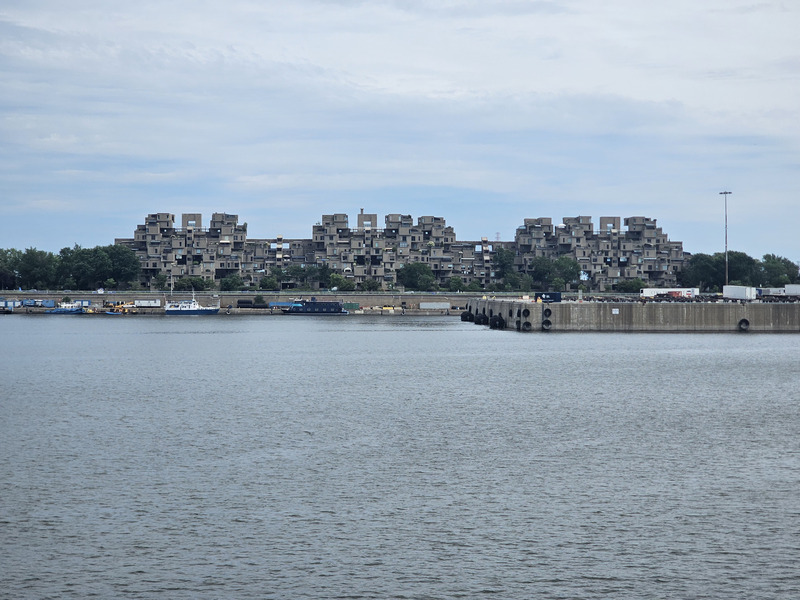 The stacked concrete apartments and terraces of Habitat 67 across the water, with boats and a quay in front.